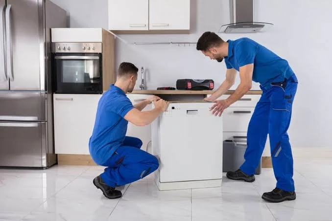 Two appliance technicians positioning a dishwasher in a home kitchen